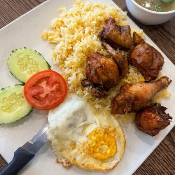 Fried chicken and rice with a fried egg, cucumber, and tomato slices on a white plate.