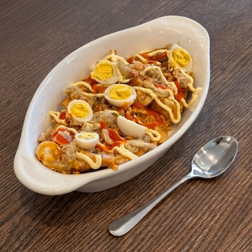 A white dish filled with sisig, topped with mayonnaise, hot sauce, and sliced boiled eggs.