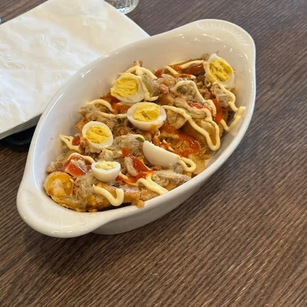 A white oval dish filled with sisig, topped with mayonnaise, ketchup, and sliced hard-boiled eggs.