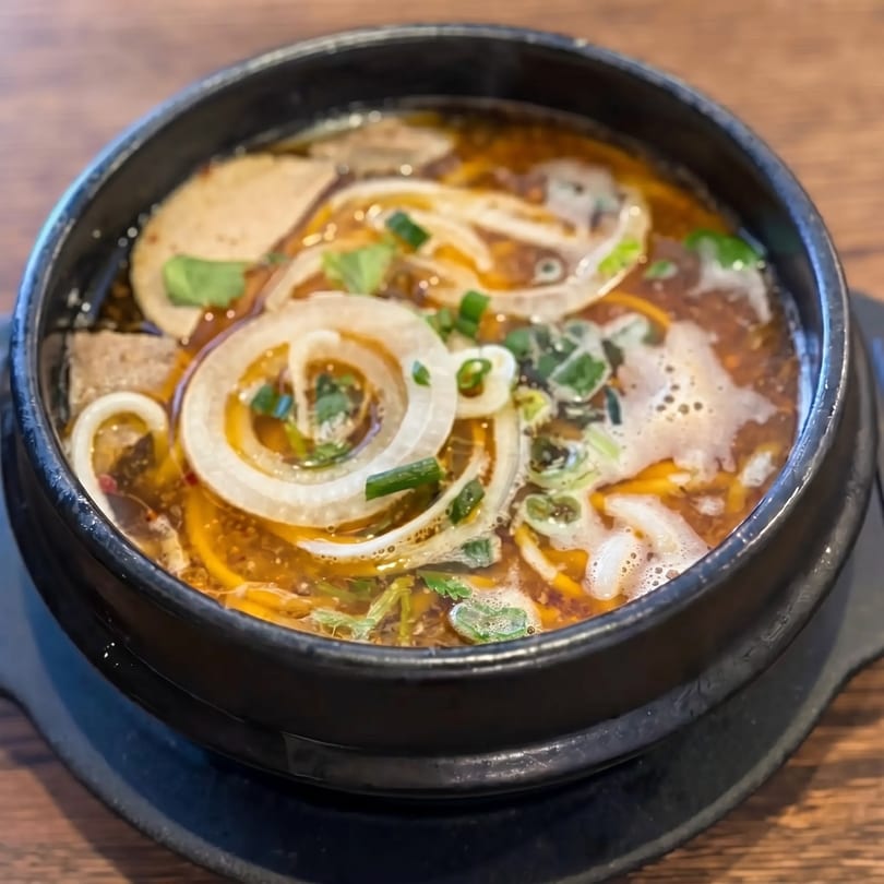 Spicy Vietnamese noodle soup with sliced onions, green onions, and meat in a black bowl.
